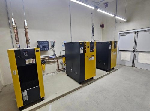 Three yellow and black industrial machines in a clean, well-lit room with pipes and control panels.