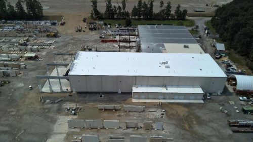 Aerial view of a large industrial warehouse with construction materials and equipment nearby.