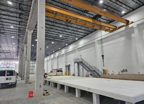 Large industrial warehouse with a crane, vehicles, raised platform, and a metal staircase.