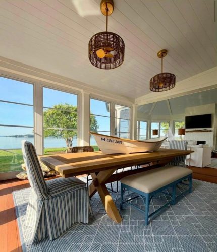 Sunlit dining area with a wooden table, striped chairs, and boat decoration, overlooking a lake.