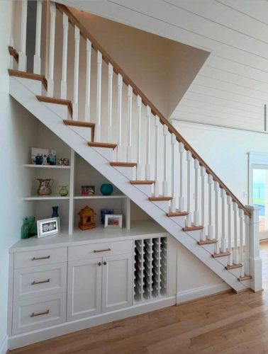 White staircase with wooden steps; built-in shelves, cabinets, and a wine rack underneath.