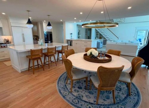 Modern kitchen and dining area with wooden chairs, round table, and blue rug on light wood flooring.