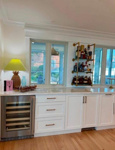 White kitchen with a wine fridge, pineapple lamp, bar shelves, and patio doors overlooking a backyard.