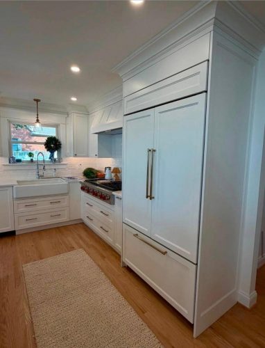 Modern kitchen with white cabinets, wood flooring, sink by the window, and a large built-in refrigerator.