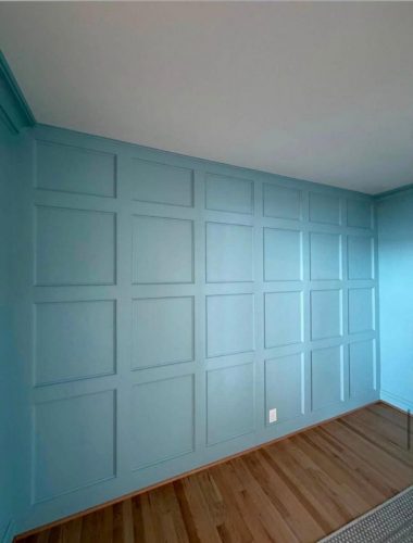 A blue accent wall with a grid pattern of square panels and wooden floor below.